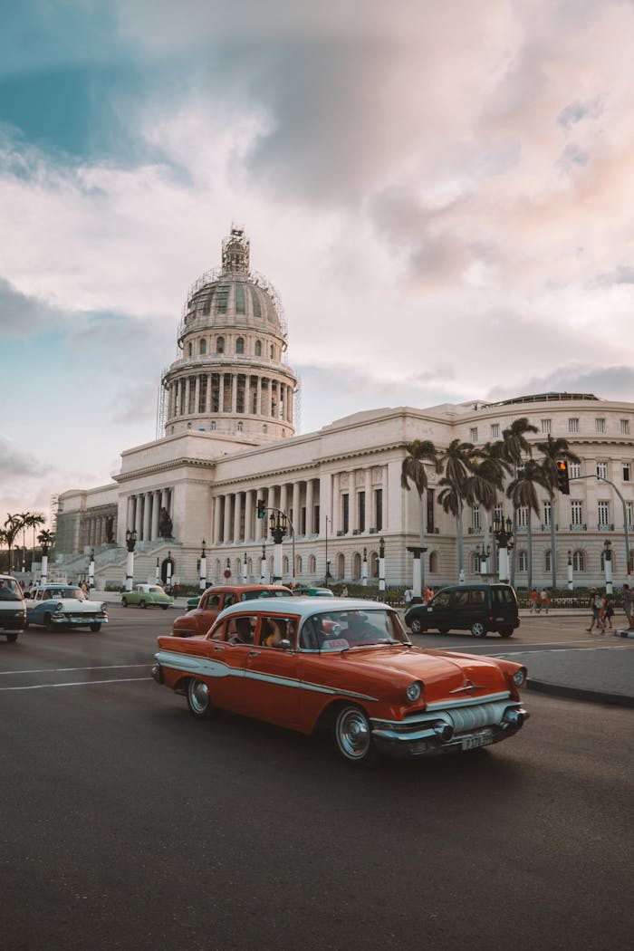 A classic car drives past the historic El Capitolio in Havana, Cuba, under a dramatic sky.